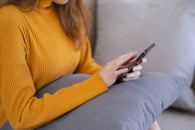 Mulher asiática enviando mensagens de texto verificando mídias sociais segurando smartphone em casa Conversando com namorado ou amigo