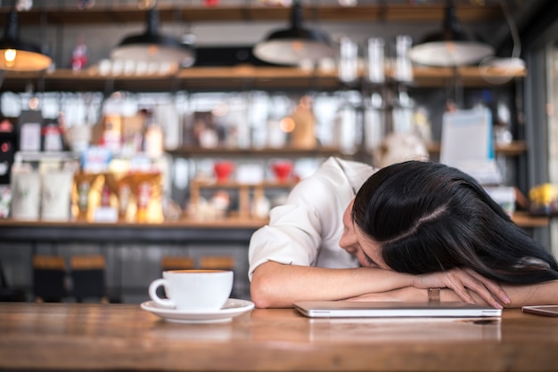 Mulher asiática está descansando e dormindo em uma loja de café porque ela está cansada de trabalhar