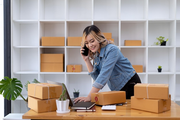 Mulher asiática está falando ao telefone com um cliente para confirmar um pedido, ela é dona de uma loja online, embala e envia através de uma empresa de transporte privada. Venda online e conceitos de compras online.