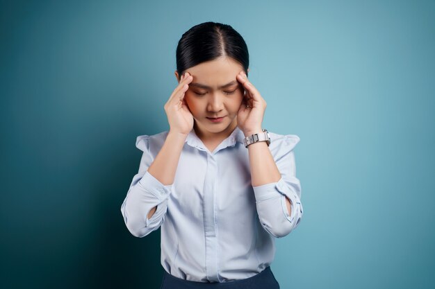Mulher asiática estava doente com dor de cabeça tocando sua cabeça isolada em azul.