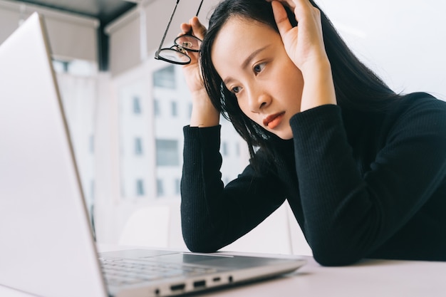 mulher asiática estressada trabalhando em casa em um laptop parecendo preocupada, cansada e oprimida