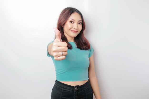 Mulher asiática excitada vestindo camisa azul dá polegares para cima gesto de aprovação isolado por fundo branco