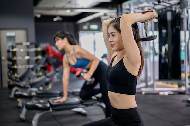 Mulher asiática exercício e estilo de vida no ginásio de fitness. Treino de mulher desportiva com treinador e peso do haltere. Bem-estar e saúde para a musculação.