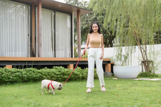 Foto mulher asiática feliz a brincar com um cãozinho no quintal.