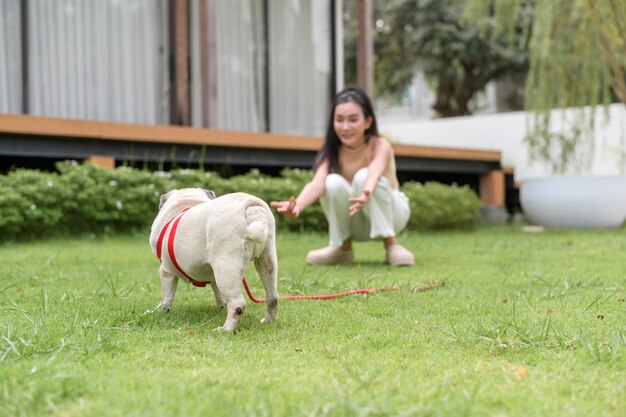 Foto mulher asiática feliz a brincar com um cãozinho no quintal.