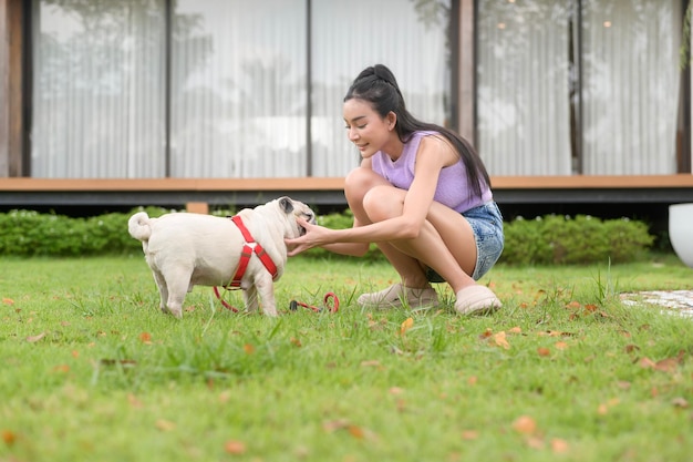 Mulher asiática feliz a brincar com um cãozinho no quintal.