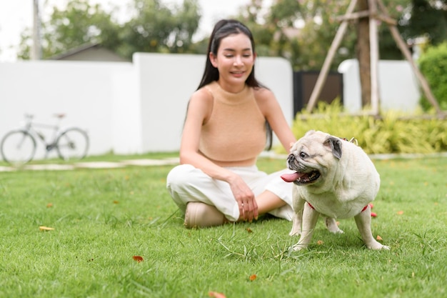 Mulher asiática feliz a brincar com um cãozinho no quintal.