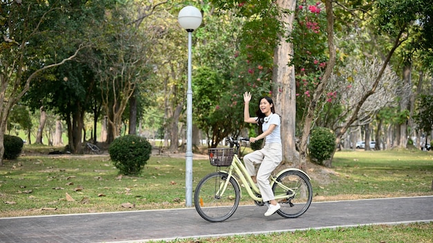 Mulher asiática feliz anda de bicicleta na ciclovia no parque público no fim de semana