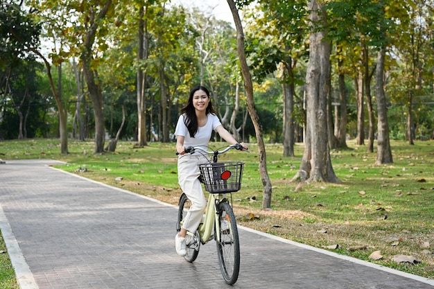 Mulher asiática feliz andando de bicicleta no parque no fim de semana gosta de fazer atividades ao ar livre