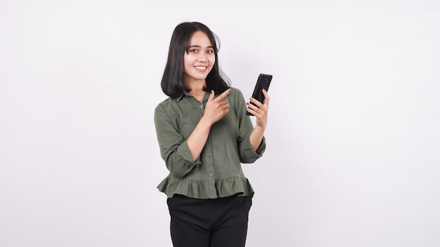 Mulher asiática feliz apontando o telefone em uma parede branca e isolada
