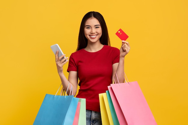 Mulher asiática feliz com cartão de crédito de telefone e sacos de compras