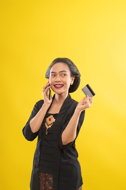 Mulher asiática feliz com kebaya usando o telefone, comprando com cartão de crédito