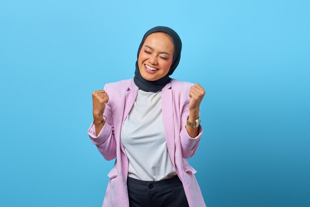 Mulher asiática feliz comemorando o sucesso com expressão de riso sobre fundo azul