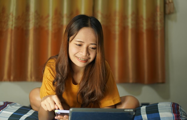 Mulher asiática feliz depois de ver o lucro do computador na cama trabalhando em casa