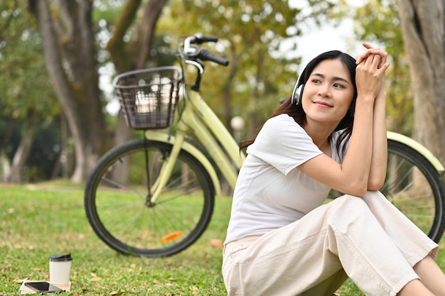 Mulher asiática feliz e relaxada ouvindo música e descansando depois de andar de bicicleta no parque público