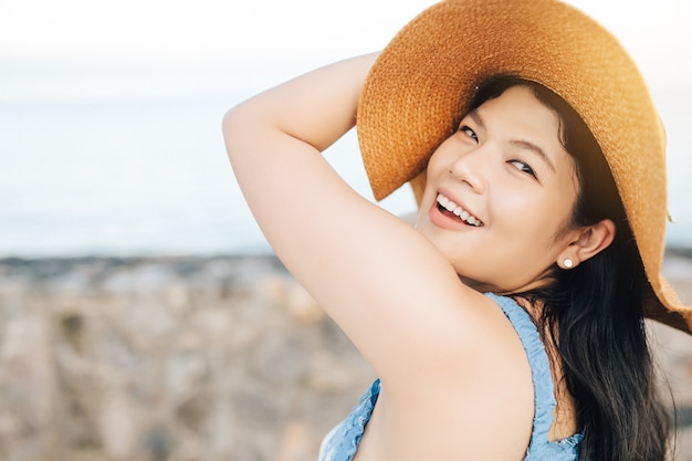 Mulher asiática feliz e sorridente, curtindo a praia e olhando para a câmera no verão