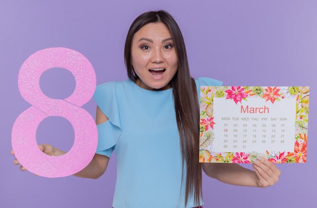 Mulher asiática feliz e surpresa segurando o calendário de papel e o número oito