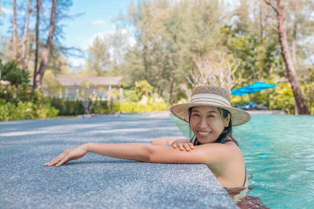 Mulher asiática feliz em maiô vermelho e chapéu de palha relaxa na piscina olhe para a câmera Phangnga Tailândia