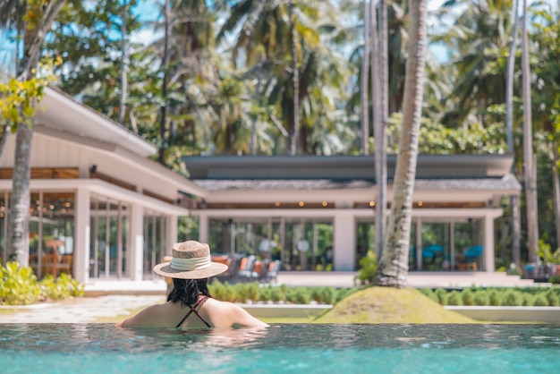 Mulher asiática feliz em maiô vermelho e um chapéu de palha relaxando na piscina, veja a vista em Phangnga Tailândia