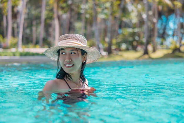 Mulher asiática feliz em traje de banho vermelho e um chapéu de palha relaxando na piscina, veja a vista em phangnga tailândia