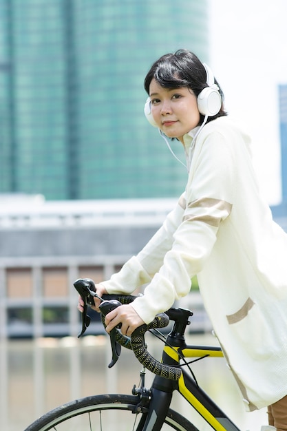 Mulher asiática feliz ouvindo música na bicicleta perto do lago