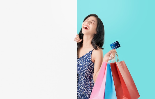 Mulher asiática feliz segurando sacolas com cartão de crédito e mostrando o quadro em branco.