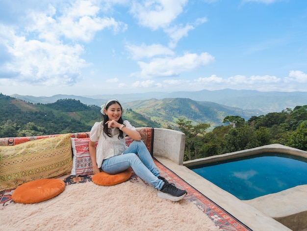 Mulher asiática feliz senta e relaxa na varanda com vista para a montanha e céu azul nublado em Doi Chang, atração turística em Chiang Rai, Tailândia