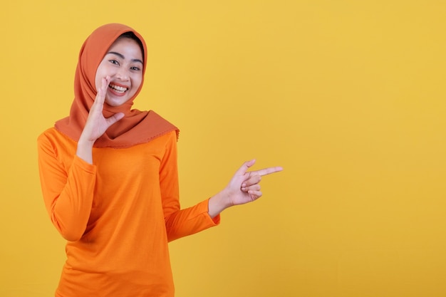 Mulher asiática feliz sorridente com o dedo apontando isolado no fundo da bandeira amarela clara usando hijab