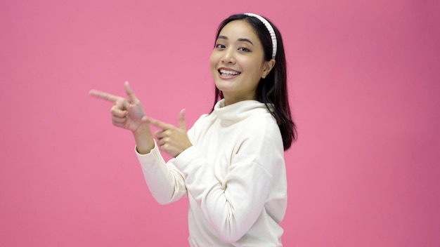 Mulher asiática feliz sorrindo e apresentando o espaço de cópia isolado no fundo rosa