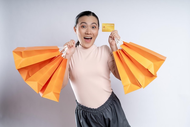 Mulher asiática feliz sorrindo segurando sacolas de compras e cartão de crédito isolado sobre fundo branco