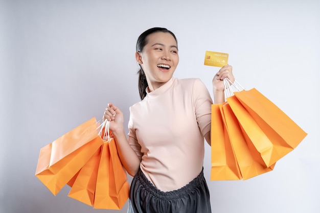 Mulher asiática feliz sorrindo segurando sacolas de compras e cartão de crédito isolado sobre fundo branco