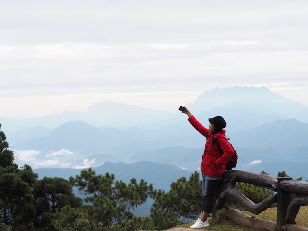 Mulher asiática feliz tirando fotos sobre a vista da montanha com fundo de névoa
