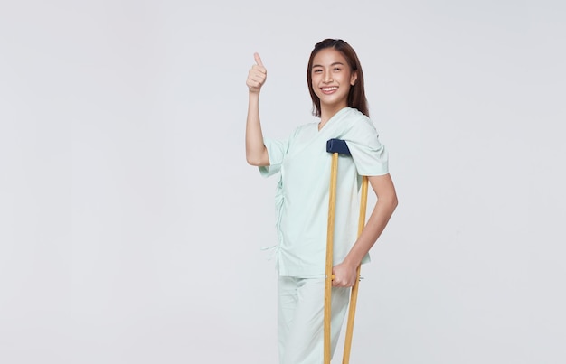 Foto mulher asiática feliz torce o pé usando muletas mostrando os polegares para cima