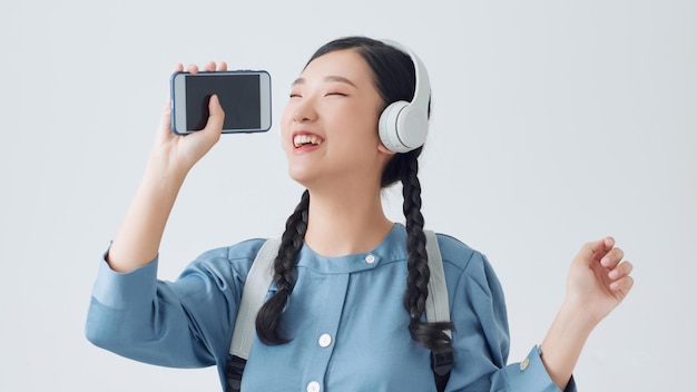 Mulher asiática feliz usando fones de ouvido ouvindo música online dançando e cantando em fundo branco isolado