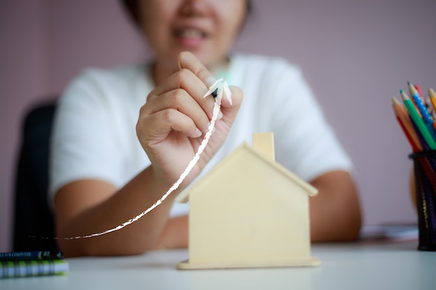 Mulher asiática feliz usando lápis desenhar forma de seta superior com metáfora de cofrinho de casa de madeira, economizando dinheiro para comprar a casa