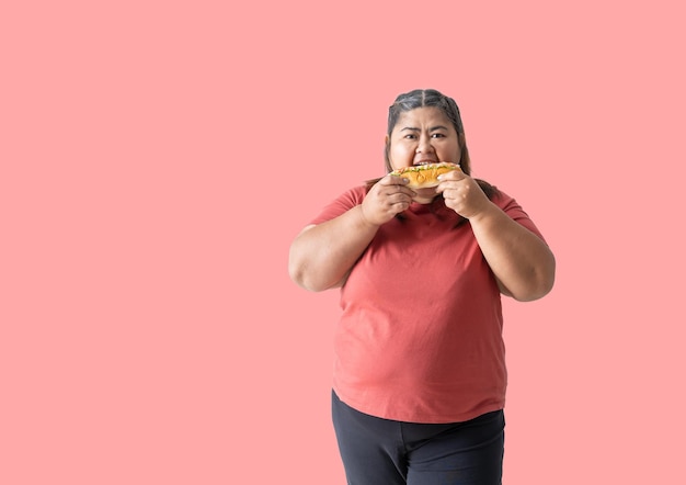 Foto mulher asiática gorda comendo hambúrguer isolada em fundo rosa