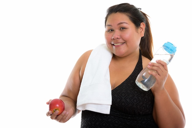 Mulher asiática gorda e feliz sorrindo enquanto segura uma maçã vermelha e uma garrafa de água