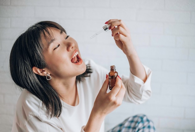 Mulher asiática gotejando óleo de CBD na boca para dormir vitaminas e suplementos de cannabis medicinal