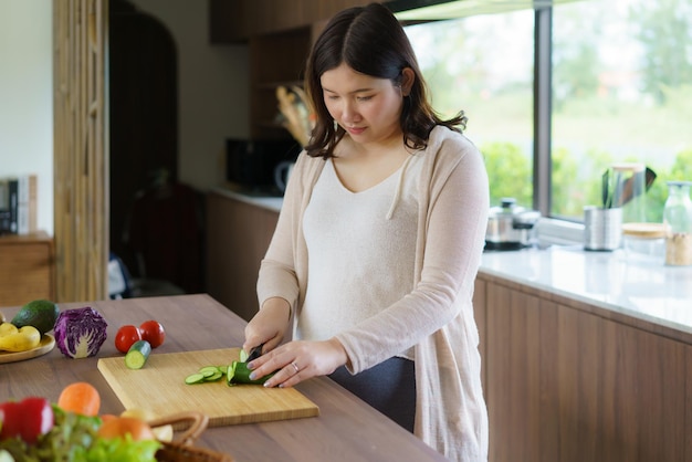 Mulher asiática grávida cortando pepino para salada verde fresca Fêmea prepara um delicioso jantar orgânico