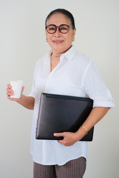 Mulher asiática idosa ativa segurando o laptop e o copo da bebida. Conceito de negócios