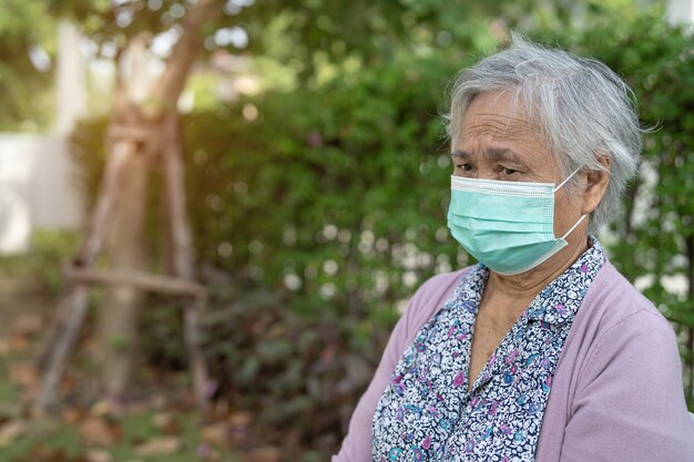 Mulher asiática idosa ou idosa usando uma máscara facial sentada no parque em casa para proteger a infecção de segurança Covid-19 Coronavirus.