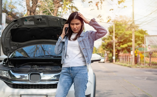 Mulher asiática irritada e usando telefone celular pedindo assistência após uma avaria de carro na rua