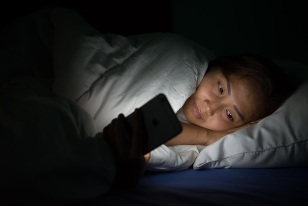 Mulher asiática joga smartphone na cama à noiteTailândia