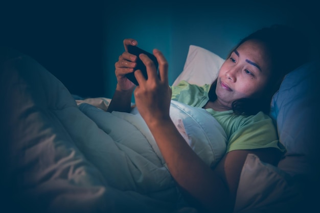 Mulher asiática joga smartphone na cama à noiteTailândiapessoasViciam mídia socialJoga internet a noite toda