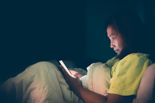 Mulher asiática joga smartphone na cama à noiteTailândiapessoasViciam mídia socialJoga internet a noite toda