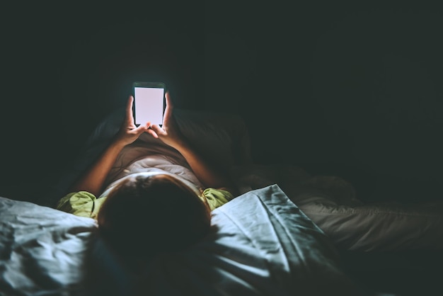 Mulher asiática joga smartphone na cama à noiteTailândiapessoasViciam mídia socialJoga internet a noite toda