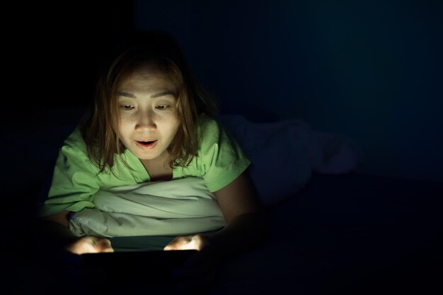 Mulher asiática joga smartphone na cama à noiteTailândiapessoasViciam mídia socialJoga internet a noite toda