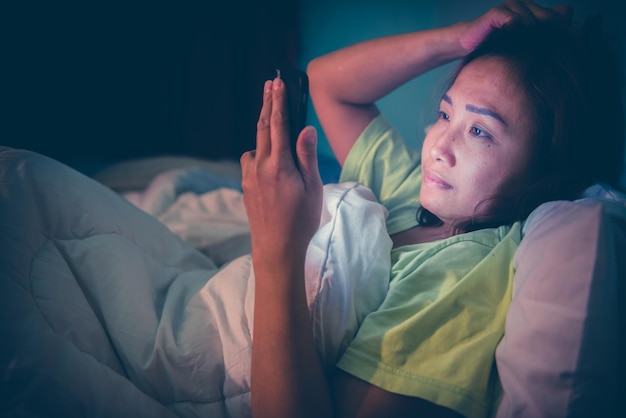 Mulher asiática joga smartphone na cama à noiteTailândiapessoasViciam mídia socialJoga internet a noite toda