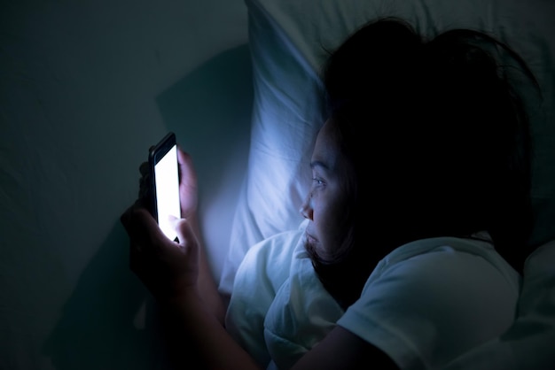 Mulher asiática jogando no smartphone na cama à noiteTailândiapessoasViciado mídia social