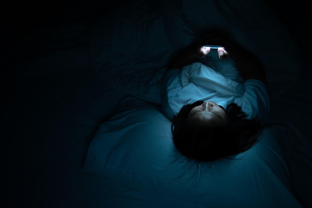 Mulher asiática jogando no smartphone na cama à noiteTailândiapessoasViciado mídia social